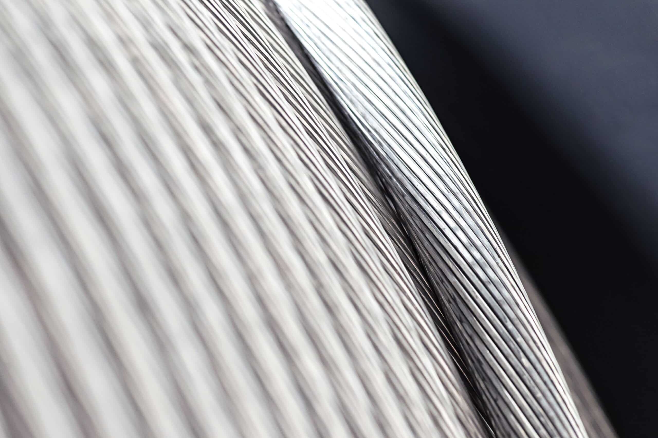 Primer plano de alambres metálicos finos enrollados en una bobina, con textura lineal y acabado brillante