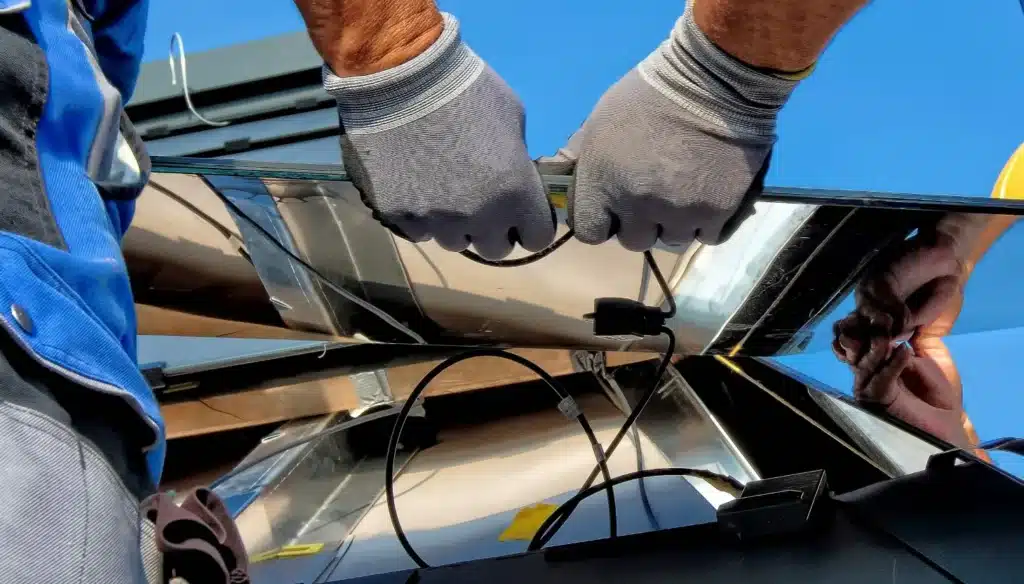 Manos con guantes conectando el cableado de un panel solar durante su instalación.